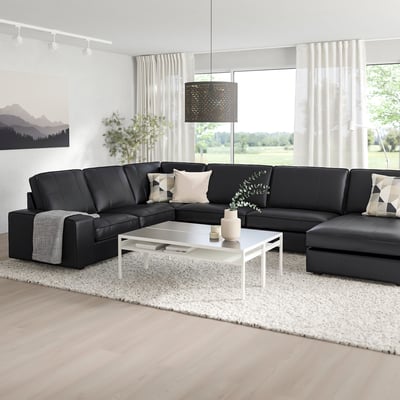 Modern living room with large black KIVIK sectional sofa, white coffee table, and large windows. Sleek, minimalist design for relaxation.