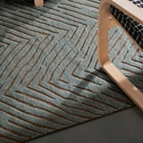 Light blue and brown patterned rug on a wooden floor; a chair leg rests on the rug, showing its purpose for floor protection and adding comfort.