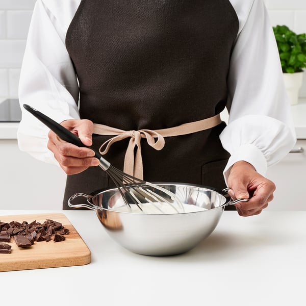 Person wearing apron uses double boiler on counter with chopped chocolate beside it.