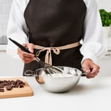 Person wearing apron uses double boiler on counter with chopped chocolate beside it.
