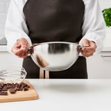 Person holds double-boiler insert over chopped chocolate, ready to melt slowly for dessert.