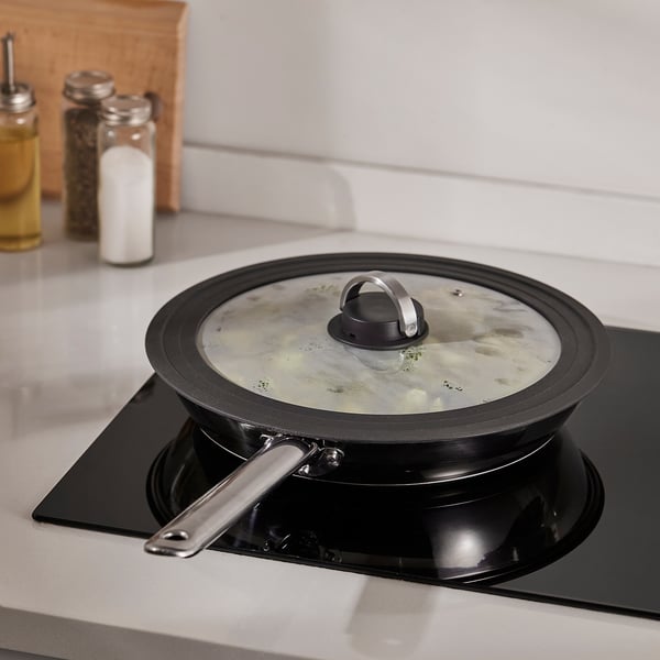 A black pot with a glass lid steams on the stove, behind bottles and containers.