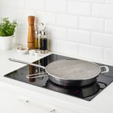 Stainless steel splatter screen over black stovetop with handles and mesh surface.