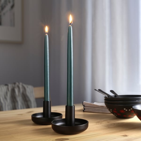 Image two lit green candles in black holders on a dining table, providing soft, ambient lighting.