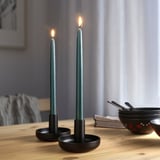 Image two lit green candles in black holders on a dining table, providing soft, ambient lighting.