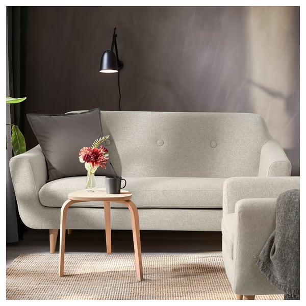 Modern grey sofa with wooden legs, a small side table, and a lamp. Brightened with a grey pillow and floral arrangement.