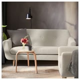 Modern grey sofa with wooden legs, a small side table, and a lamp. Brightened with a grey pillow and floral arrangement.