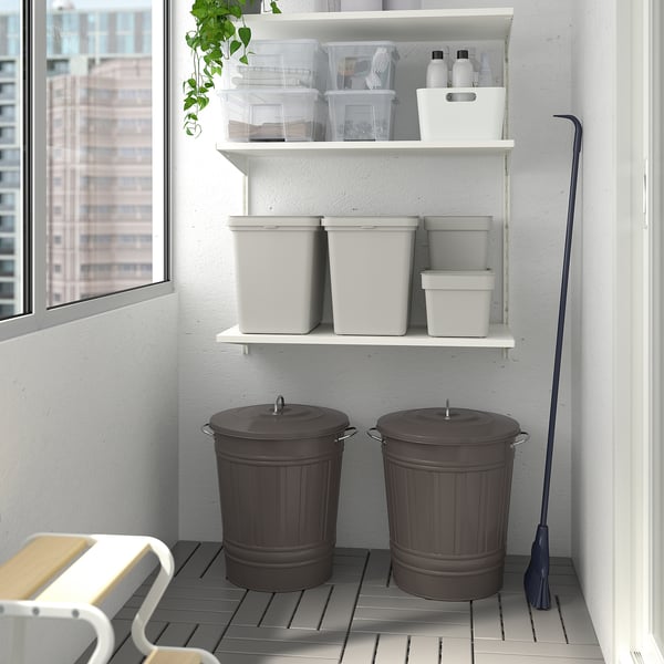 Two large grey KNODD storage bins with lids on floor, next to chair and shelves, with a blue broom.