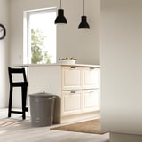 Modern kitchen with white cabinets, a wooden floor, and a grey KNODD bin. The bin has sturdy handles and a lid hook for easy access and storage.