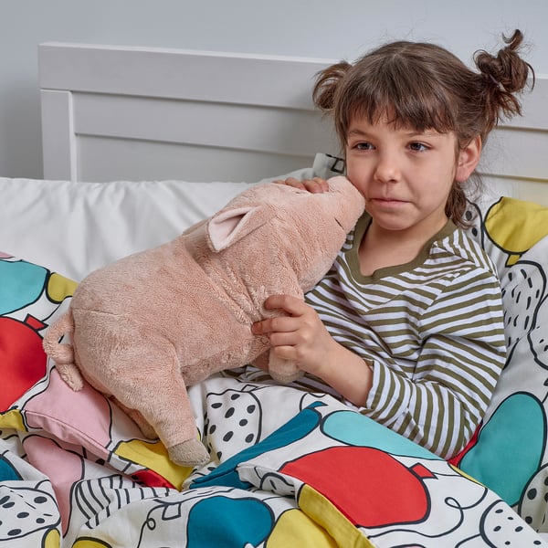 A girl holding a plush pink pig toy on a colorful bed.