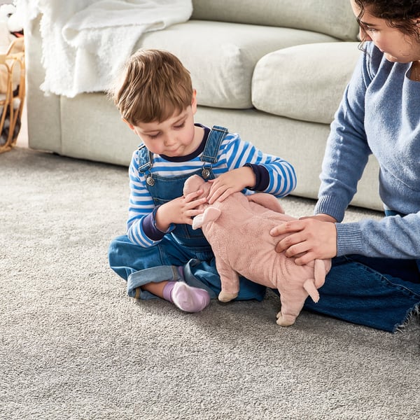 Young child plays with soft toy pig; adult assists, enhancing bonding and safety.