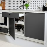 Modern kitchen with grey cabinets and white marble countertop. Open drawers reveal pots and pans storage. Backsplash has black polka dots.