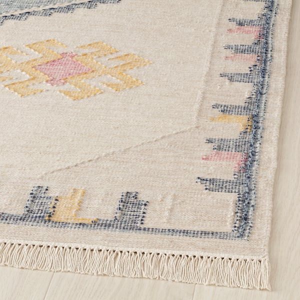 Handwoven cream rug with colorful geometric designs; fringed edges, natural wool texture.