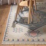 Decorative rug with geometric patterns and fringes under wooden chairs.