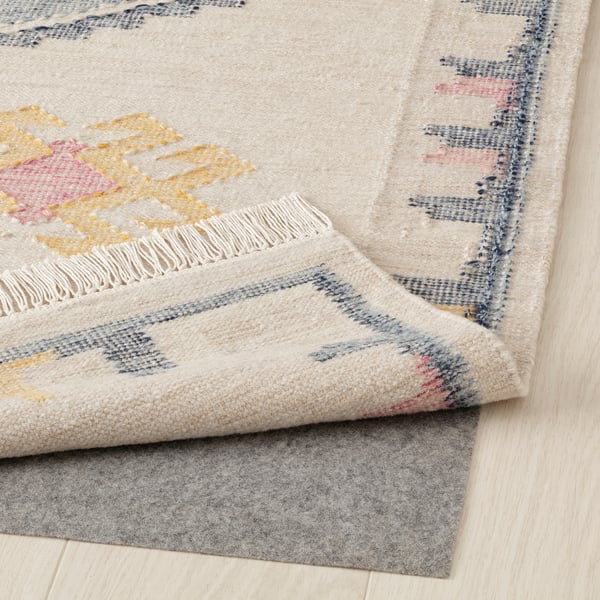 Colorful flatwoven rug with fringes, displayed on wooden floor with felt underlay.