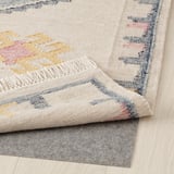 Colorful flatwoven rug with fringes, displayed on wooden floor with felt underlay.