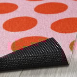 Dotted pink door mat with black textured rubber backing, folded on wooden floor.