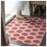 Person stepping on pink door mat with orange dots, material: rubber backing, polyester surface.