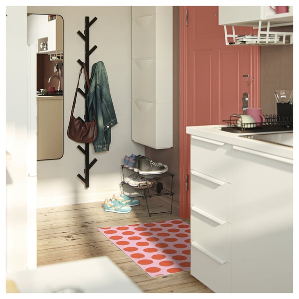 Modern entryway with a red polka dot mat, shoe rack, and black coat rack holding jacket and purse.