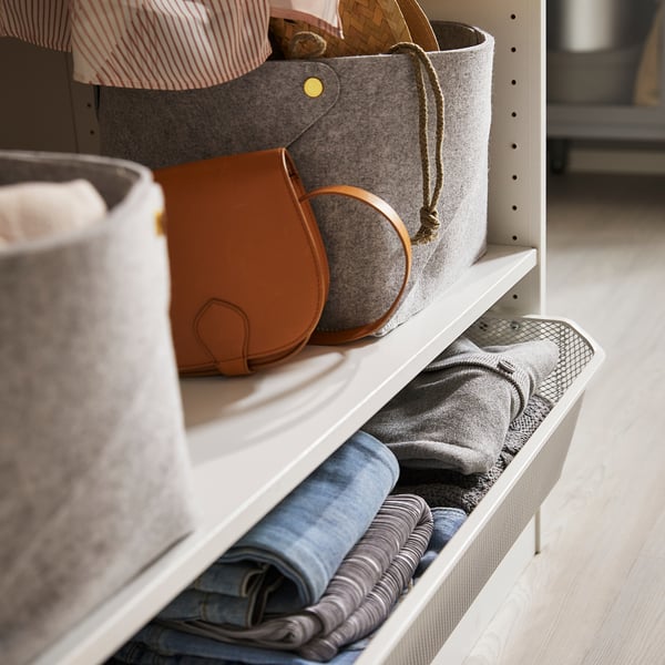 White wardrobe shelf with gray felt boxes, brown purse, and folded clothes.