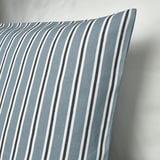 Light blue and white striped cushion cover, woven with recycled yarn, displayed against a light wall. Texture suggests cotton/jute blend.