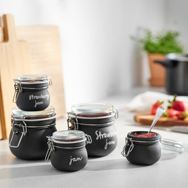 Four KORKEN jars in black, varied sizes, displayed on a table with jam inside.