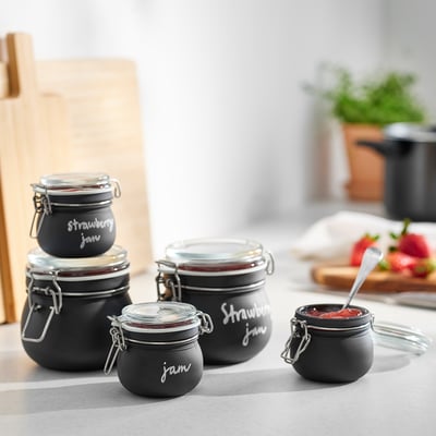 Four KORKEN jars in black, varied sizes, displayed on a table with jam inside.