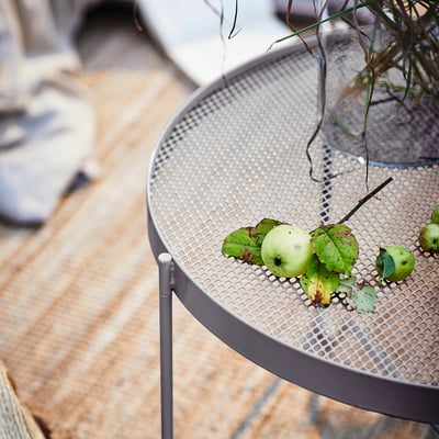 KROKHOLMEN round metal mesh table holds green apples, shown with outdoor furniture, subtle and functional design, medium size.