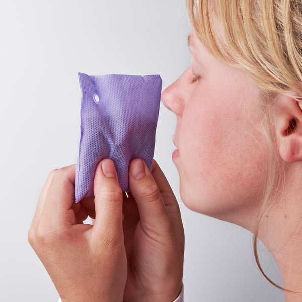 A person holds a purple lavender bag near their face, releasing a fragrant scent.