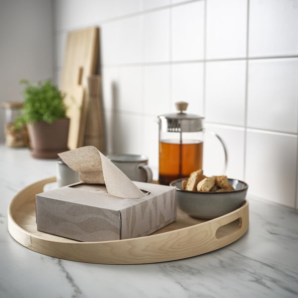 Wooden tray holds decorated box of napkins, tea pitcher, mug, and bowl of pastries on countertop.