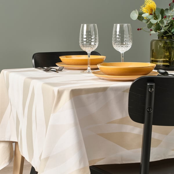 Table set for dining with two yellow bowls, two wine glasses, and silverware on white tablecloth.
