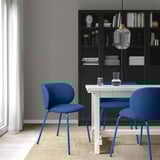 Modern dining set with blue chairs, metal legs, bookshelf, curtain, pendant light.