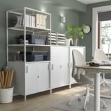 Well-organized home office with white KUGGIS storage units, gray chairs, wooden table, green plant, and wall clock.