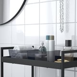 Black metal shelf in bathroom holding towels, toiletries, and a small box, ideal for organizing.
