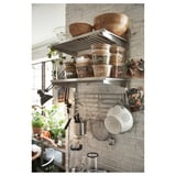 Organized kitchen with KUNGSFORS stainless steel shelves and hanging pots, displaying bowls, jars, and plants on a brick wall.