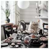 KUSTFYR black plates with spooky halloween decors, tiered cake with candles, desserts, and black chairs.