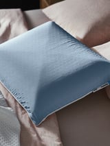 Blue ergonomic pillow with honeycomb pattern rests on a bed, showcasing its cooling side.