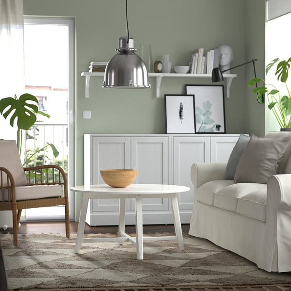 A living room with KVASTGRÄS rug, white coffee table, sofa, wicker chair, decor, and plant.