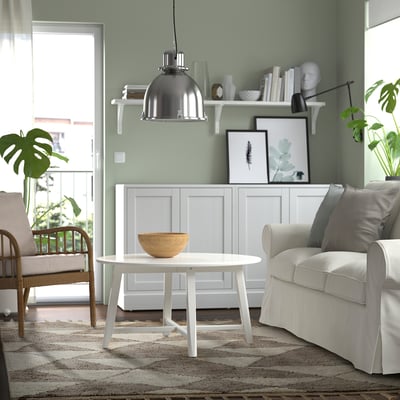 A living room with KVASTGRÄS rug, white coffee table, sofa, wicker chair, decor, and plant.