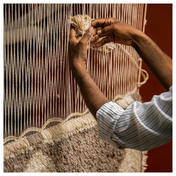 Person weaving rug, hands skillfully handling yarn.