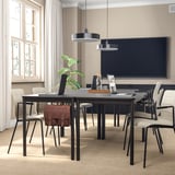 Modern conference room with dark tables, chairs, tv, and hanging lamps. Natural light and plant decor.