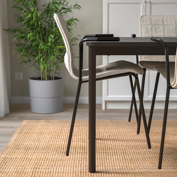 Stacked chairs with fabric seats on rug, tall plant behind.