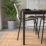 Stacked chairs with fabric seats on rug, tall plant behind.