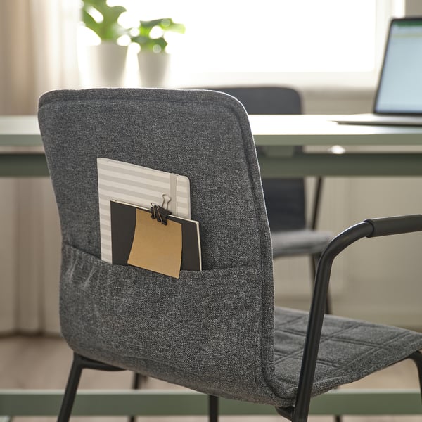 Gray office chair with cloth pocket holding notepad and paperclip, behind a desk with a laptop.