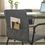 Gray office chair with cloth pocket holding notepad and paperclip, behind a desk with a laptop.