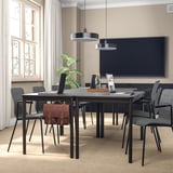Modern conference room with black chairs around a large table near a window with curtains, tv on dark wall.