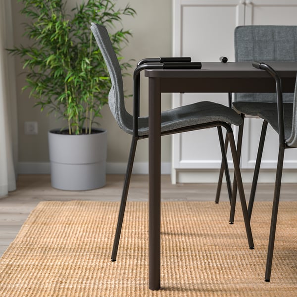 Modern conference room with stacked chairs, wood floor, area rug, and potted plant.