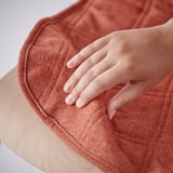 A hand grips the corner of an orange chair cover on a wooden-framed chair, showcasing its removable functionality.