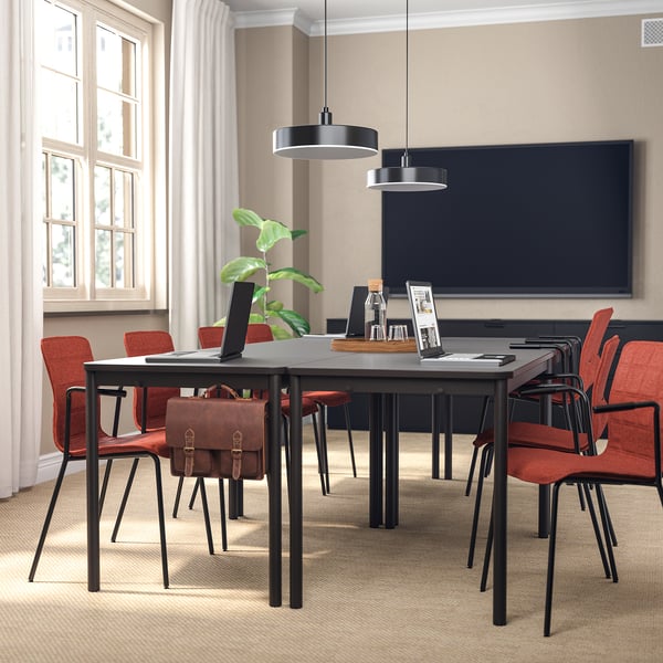 Modern conference room with black rectangular table, red LÄKTARE chairs, floating light fixtures, large white curtains, and a tv on the wall.