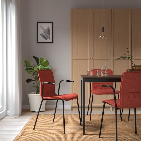 Modern dining area with red LÄKTARE chairs, dark metal frames, and wooden cabinets. Light fixture hangs over rectangular table with clear vases.